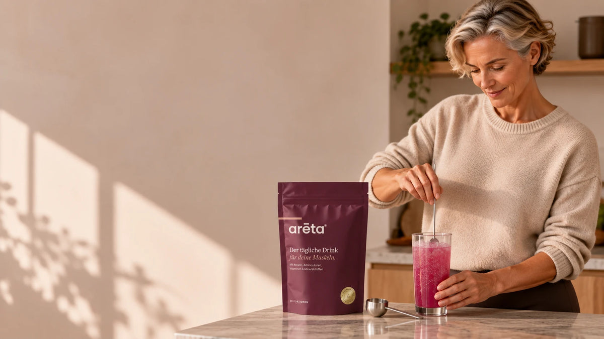 Frau rührt in ihrer Küche die arēta Tagesformel in ein Glas Wasser, der Beutel steht daneben